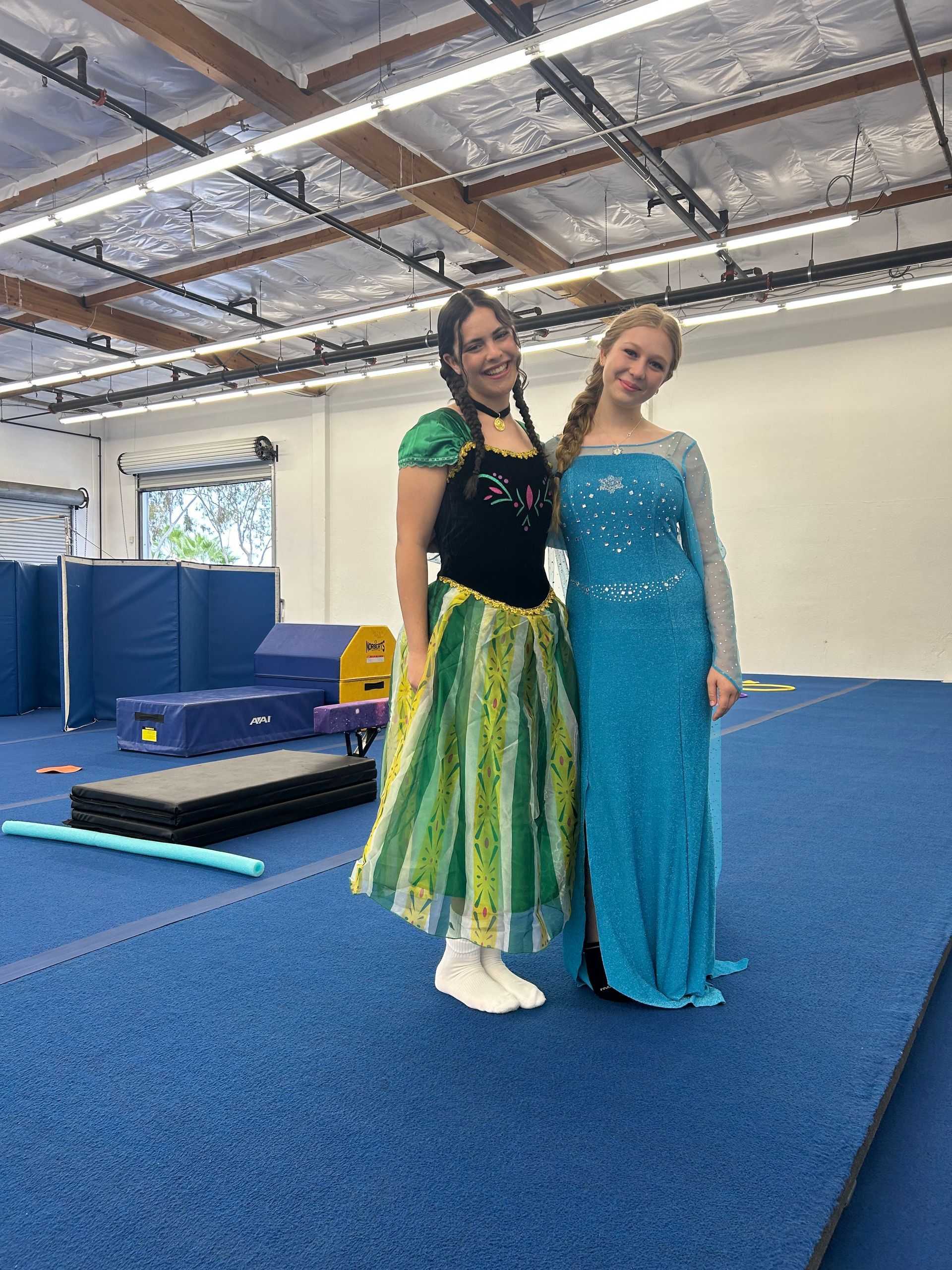 Two girls in party hats, one blowing up a purple balloon, smiling outdoors.
