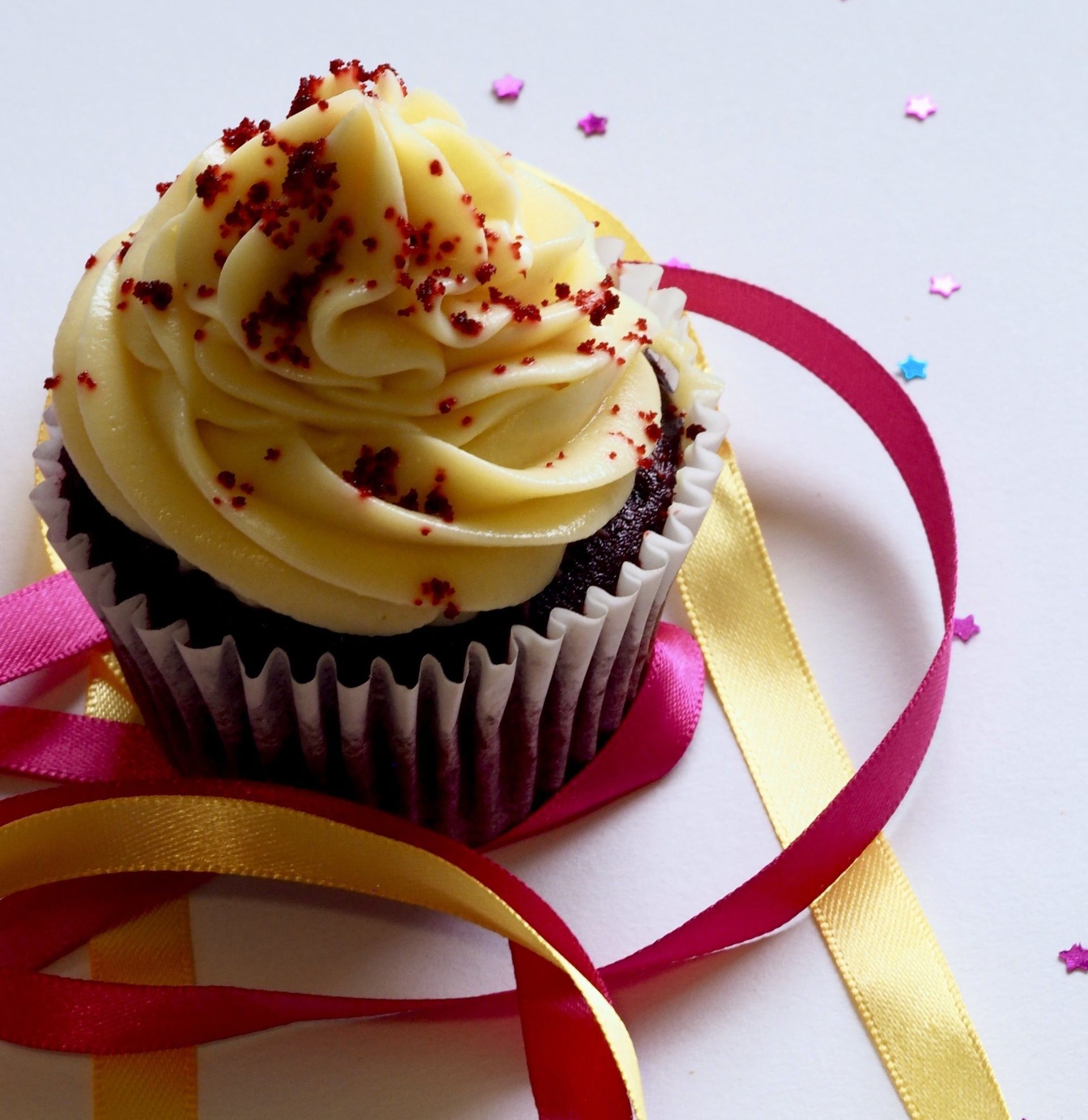 Red velvet cupcake with yellow frosting and sprinkles, ribbon streamers.
