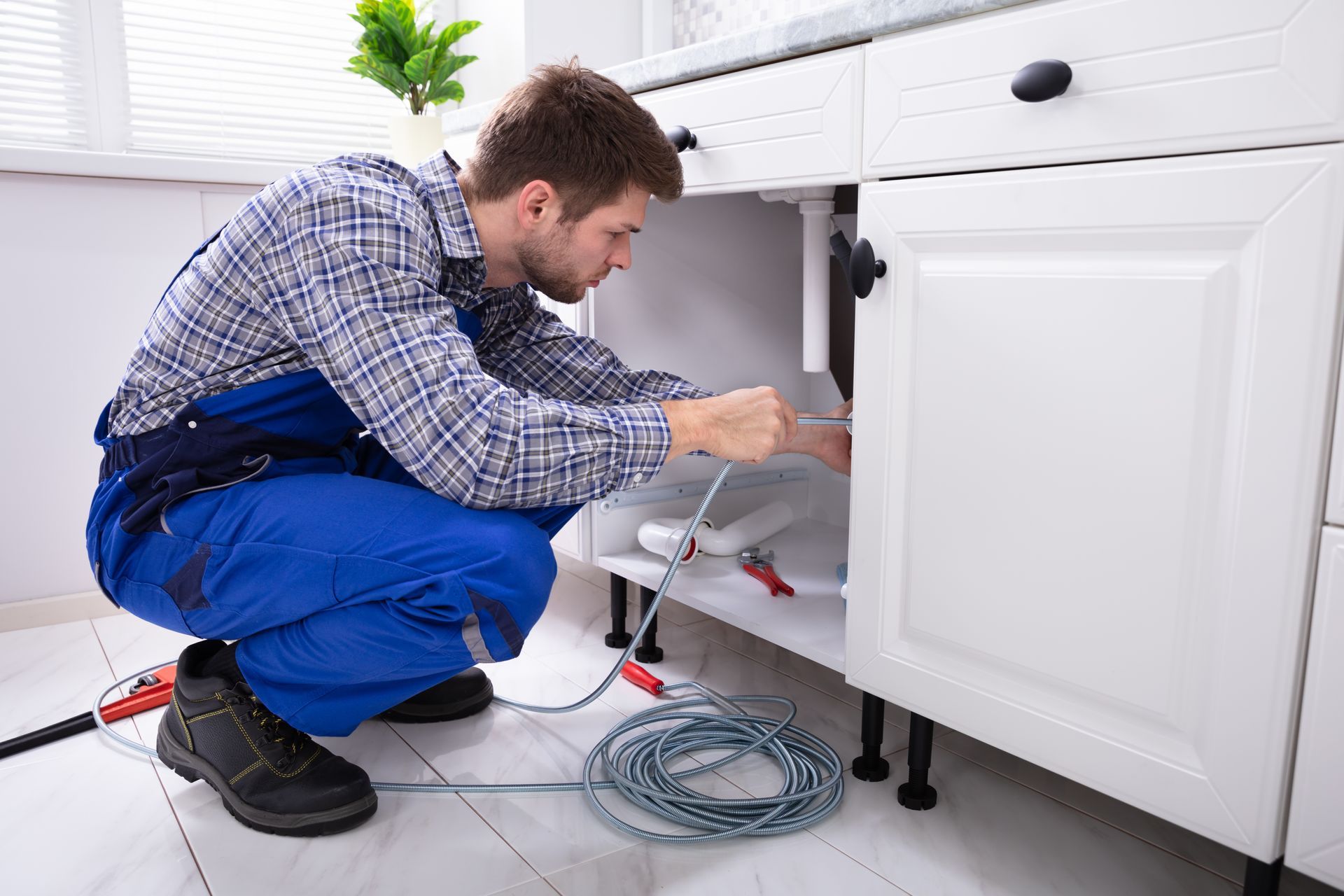 A plumber uses a snake for professional kitchen plumbing service in a residential home. A plumber uses a snake for professional kitchen plumbing service in a residential home.