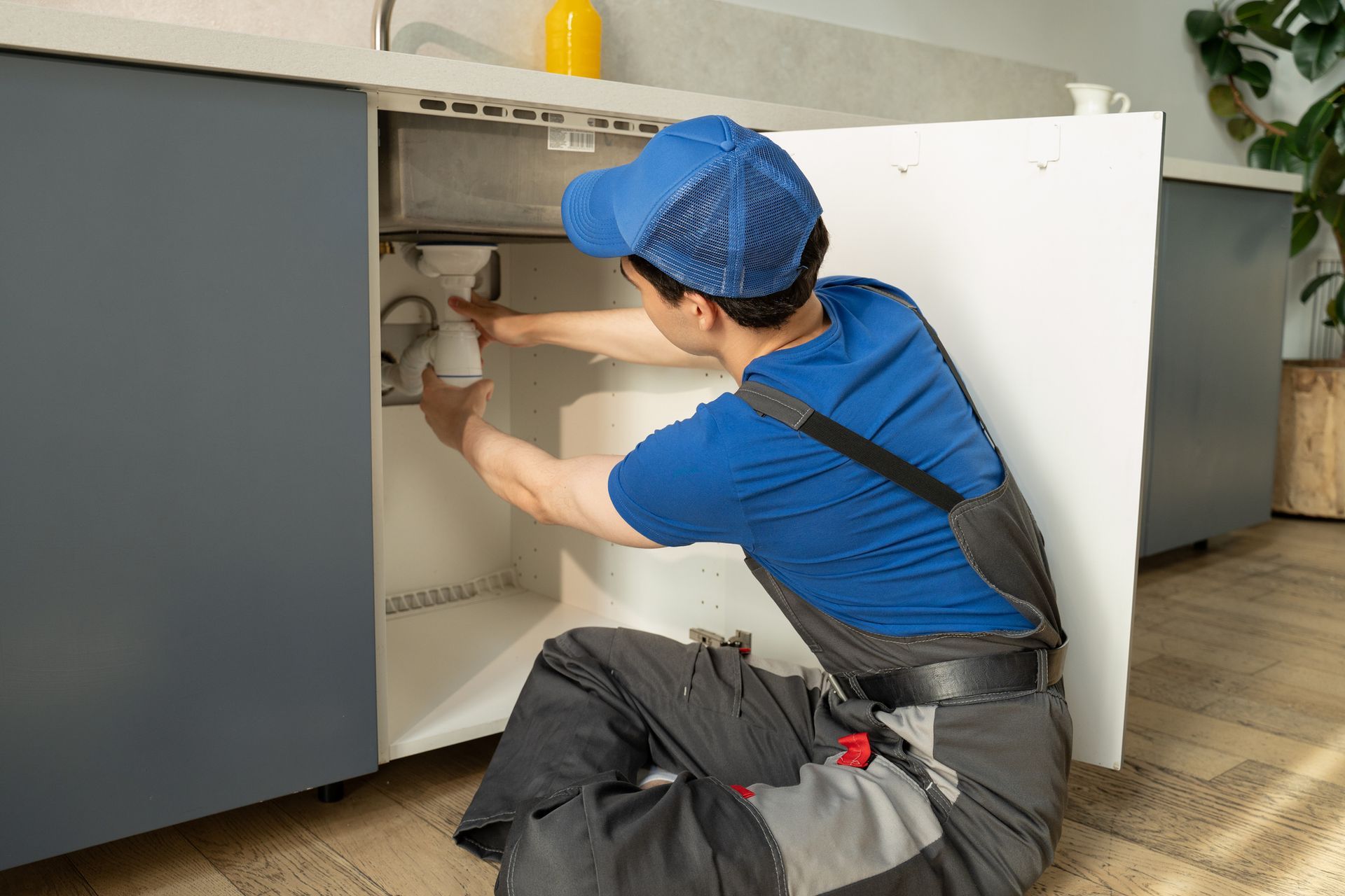 A man is adjusting the pipe under a kitchen sink.