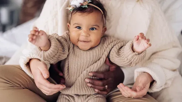 Small baby in brown sweater with hands holding it.