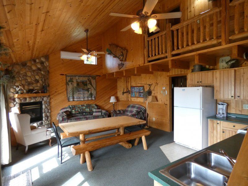 Rustic wooden cabin kitchen and dining area with table, chairs, white fridge, and sink