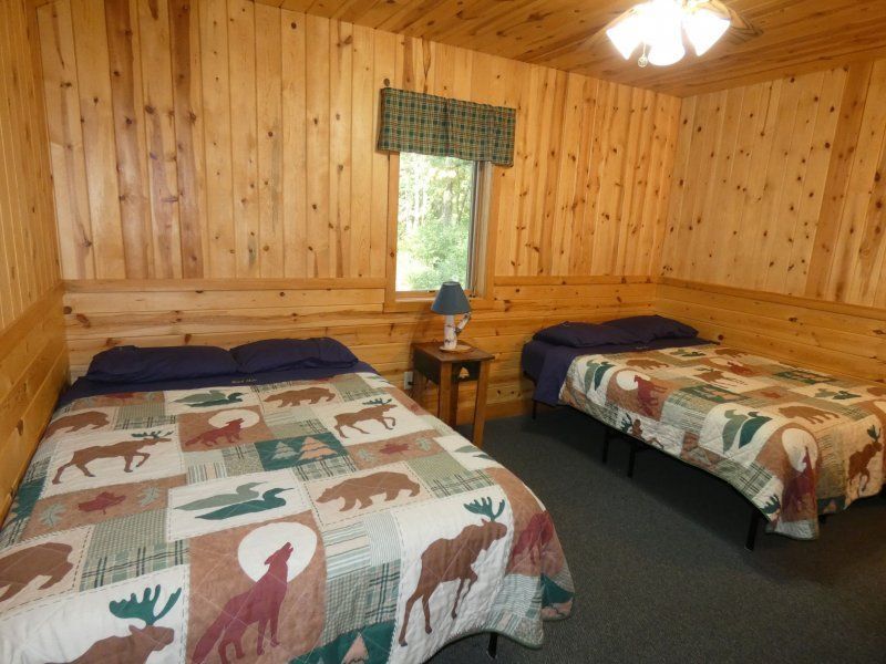 Wood-paneled cabin room with two beds, a nightstand, and a window with green valance.