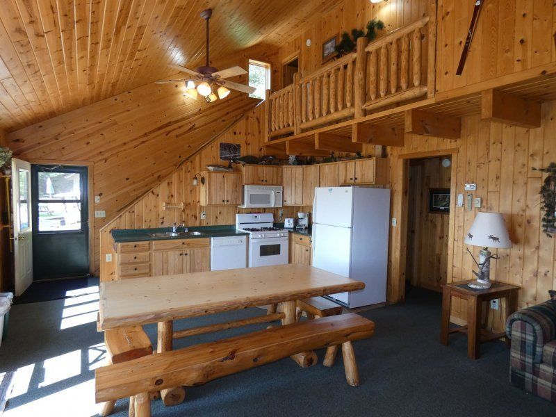 Wood-paneled cabin kitchen and dining area with loft, white appliances, and a long wooden table