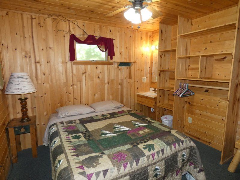 Cozy wood-paneled bedroom with a bed, shelves, lamp, and small window
