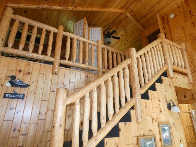 Wooden cabin interior with log staircase, balcony railing, and warm wood-paneled walls