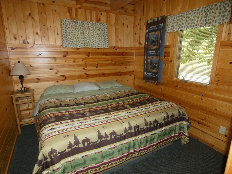 Cozy log cabin bedroom with a bed, wooden walls, window, and side table lamp
