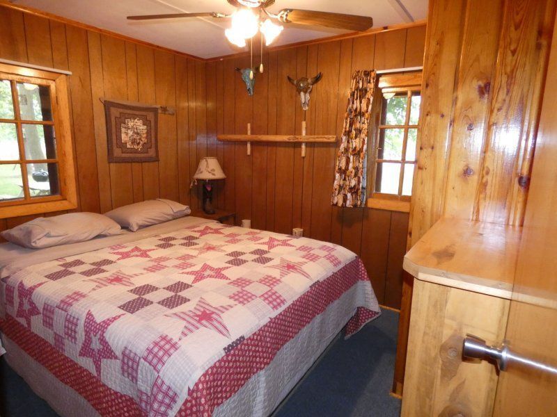 Wood-paneled bedroom with a double bed, quilted blanket, and ceiling fan under warm lighting