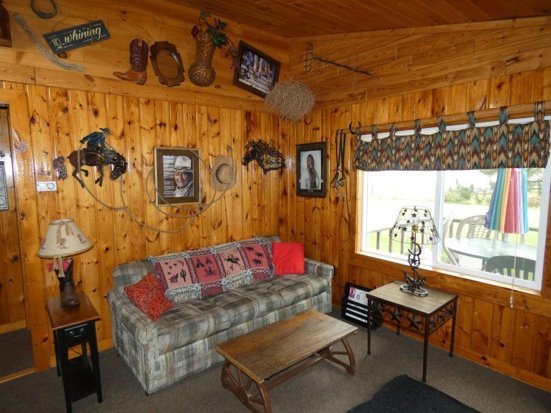 Wood-paneled living room with plaid sofa, coffee table, lamp, and large window with curtains
