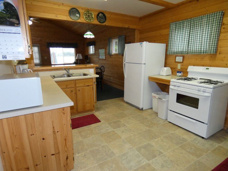 Wood-paneled kitchen with white appliances, light cabinets, and tiled floor