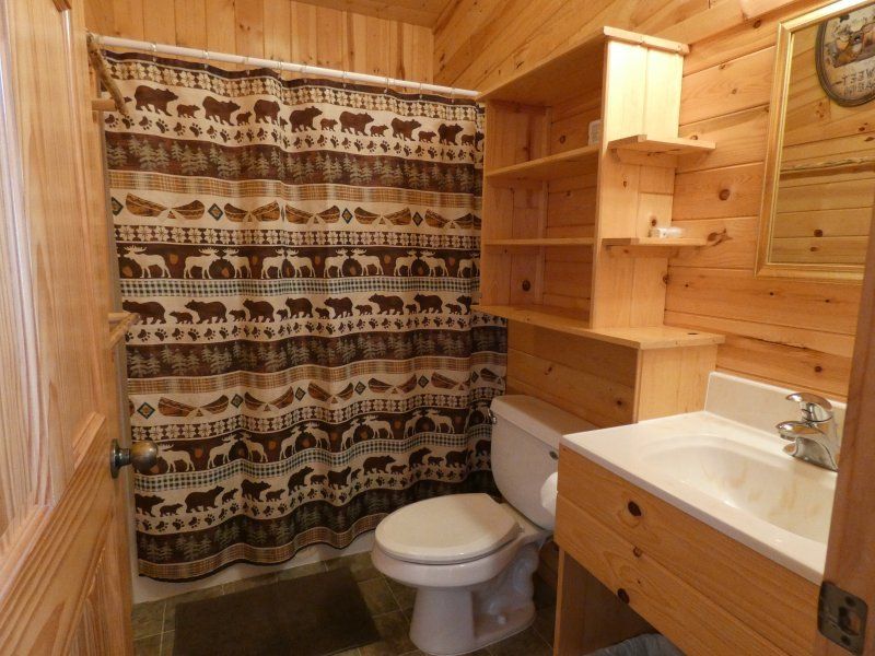 Small wood-paneled bathroom with toilet, sink, shower curtain, and shelves above the toilet.