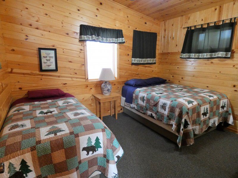 Cozy wood-paneled bedroom with two twin beds, patterned quilts, and three curtained windows