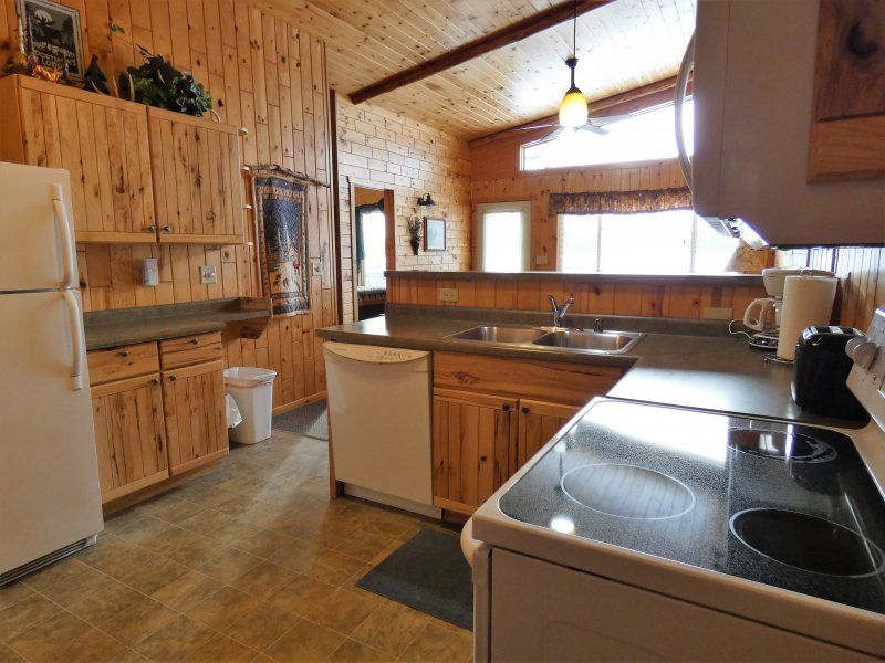 Rustic wooden kitchen with white appliances, black stove, and window over the sink