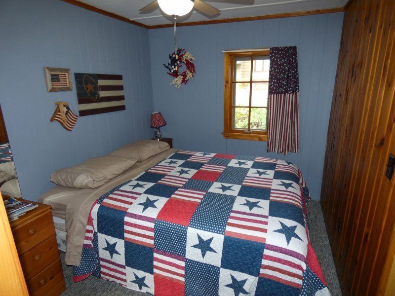 Small bedroom with a patchwork quilted bed, blue walls, wood trim, window, and dresser