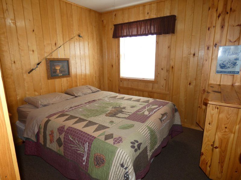 Wood-paneled bedroom with a quilted bed, window, and framed wall art