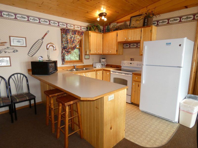 Cozy wooden kitchen with island, stools, white appliances, and wall decor in a cabin-style interior