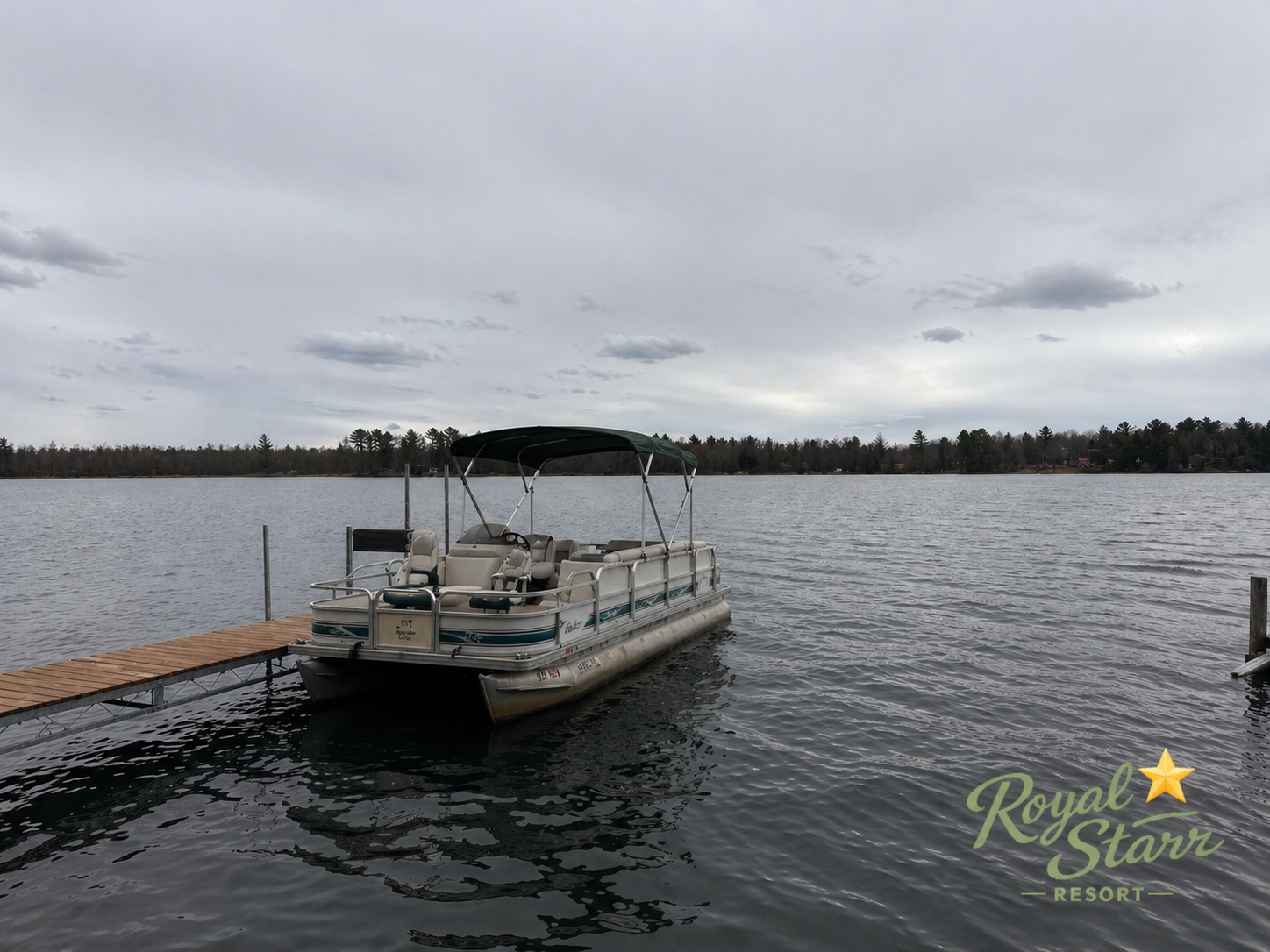 Pontoon boat docked on a calm lake under a cloudy sky