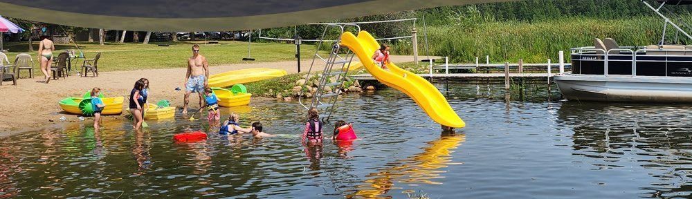Children play in a pond with colorful floats and a yellow slide near the shore.