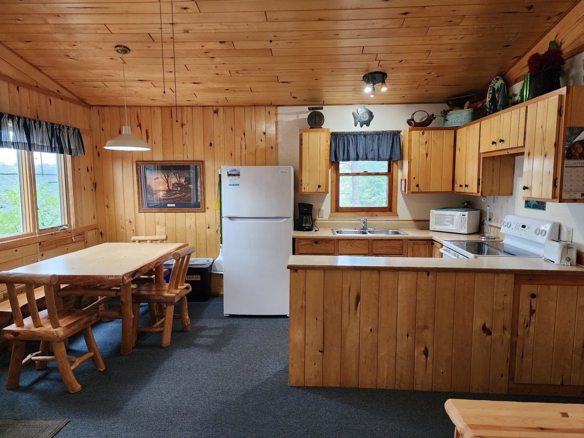 Wood-paneled kitchen with white appliances, wooden table, and window over the sink