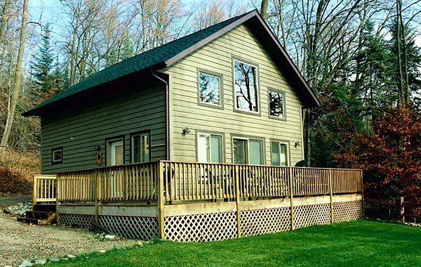 Green house with a wooden deck and lattice skirting, set in a wooded yard.