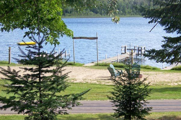 Lakeside dock with chairs and a bench, framed by trees and a sandy shoreline