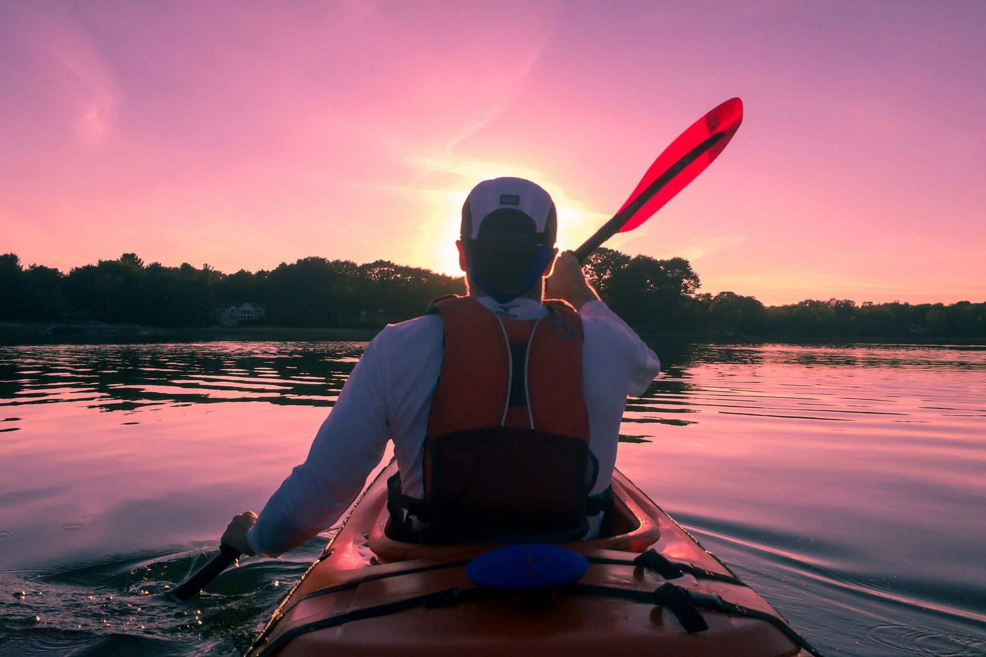 Kayaker paddling on calm water at sunset, with pink sky and silhouetted shoreline
