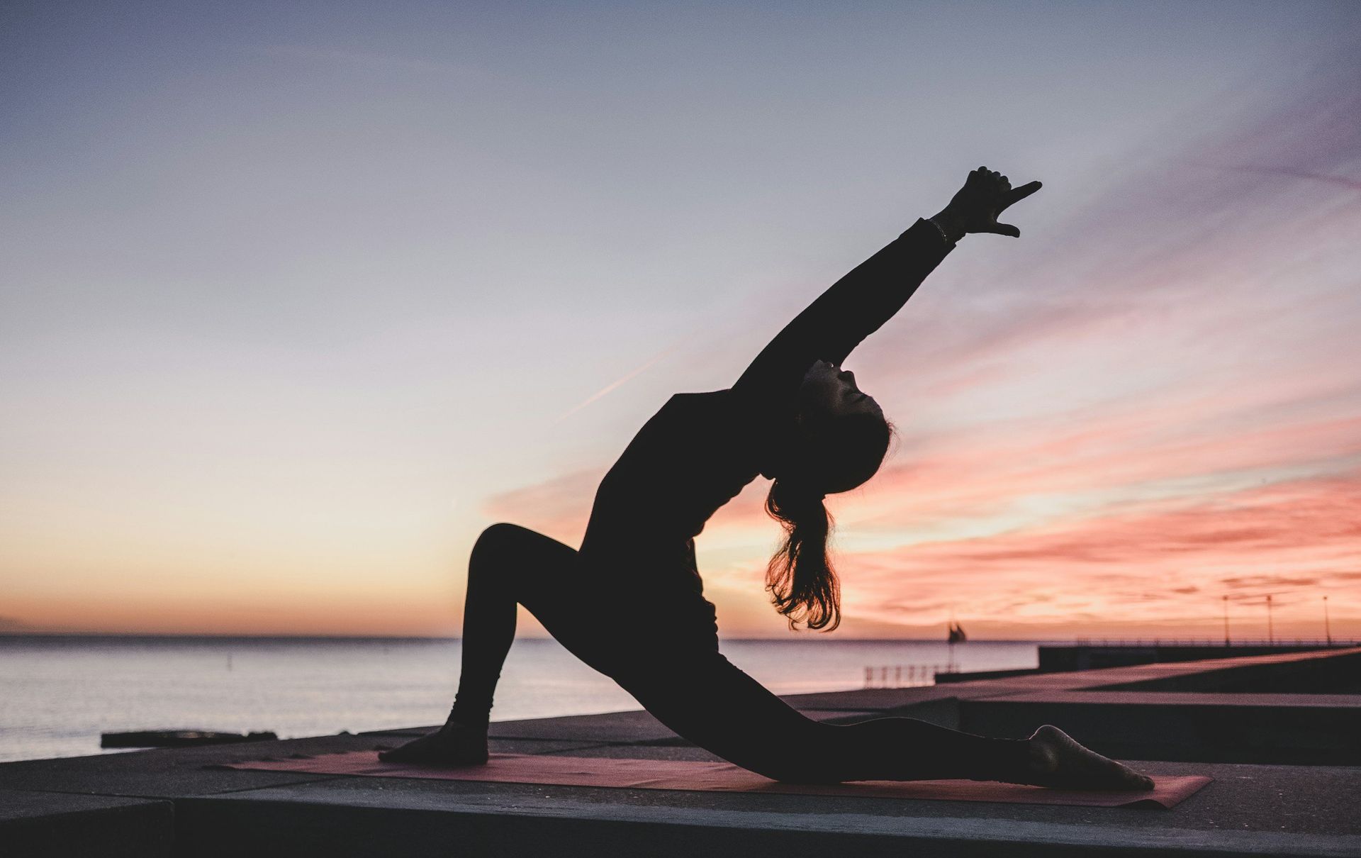 Person doing a yoga backbend pose on a beach at sunset.