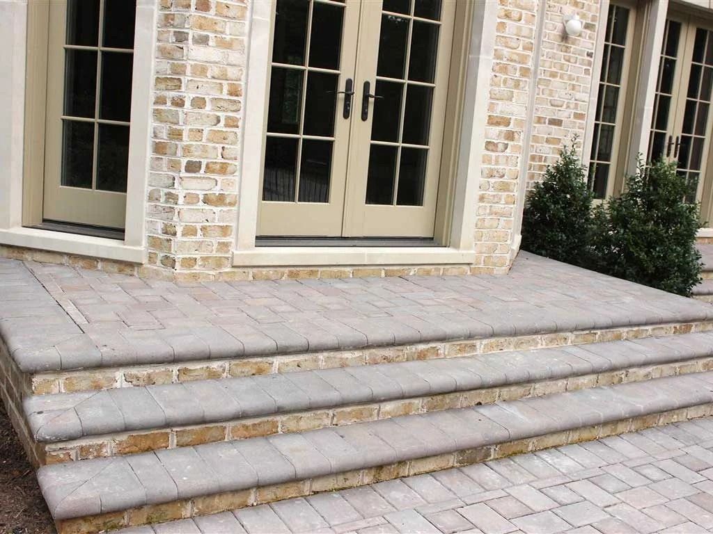 Stone steps leading to a tan brick house entrance with double doors and potted shrubs