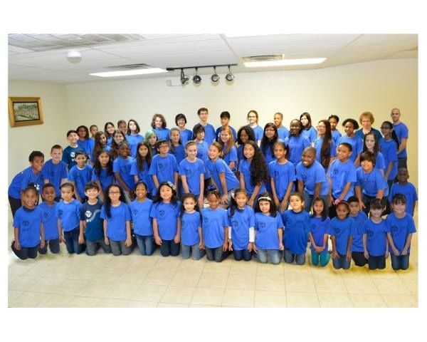 A large group of children wearing blue shirts are posing for a picture
