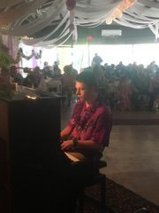 A man is sitting at a piano in a room with a crowd of people.