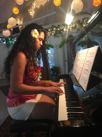 A woman is sitting at a piano with a flower in her hair.