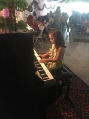 A little girl is playing a piano in front of a crowd.