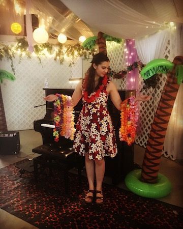 A woman in a hawaiian dress is standing in front of a piano