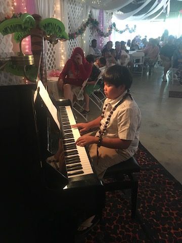 A young boy is playing a piano in a room at a party.