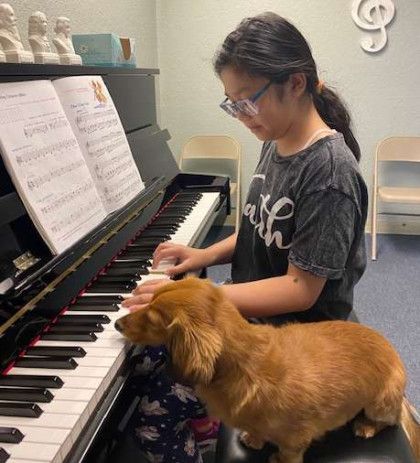 A woman is playing a piano with a dog sitting next to her.