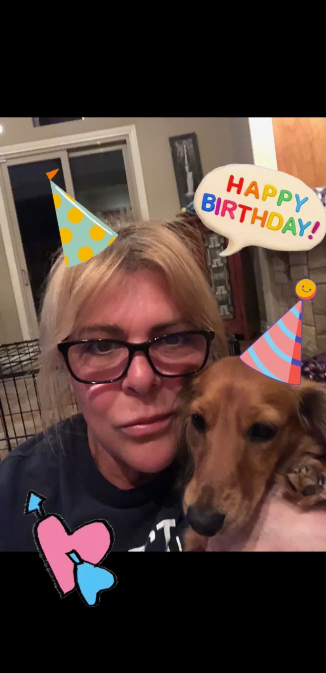 A woman wearing glasses and a birthday hat is holding a dog.