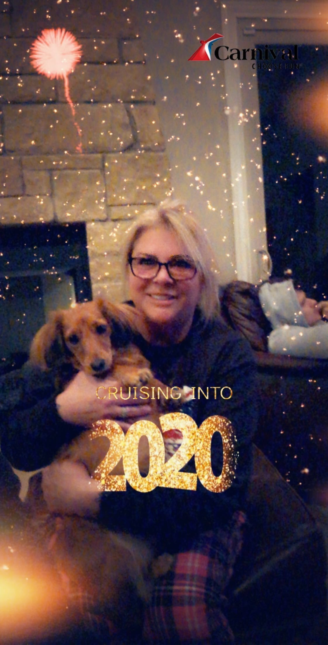 A woman is holding a dog in her arms in front of a fireplace.