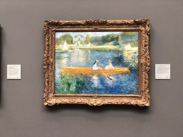 A painting of two people in a boat on a river hanging on a wall.