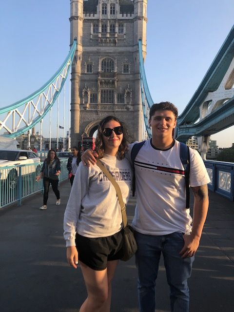 A man and a woman are posing for a picture in front of a bridge.