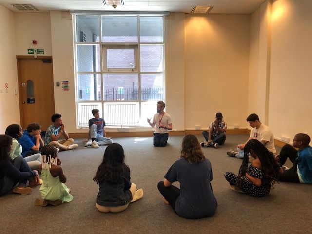 A group of people are sitting in a circle on the floor in a room.
