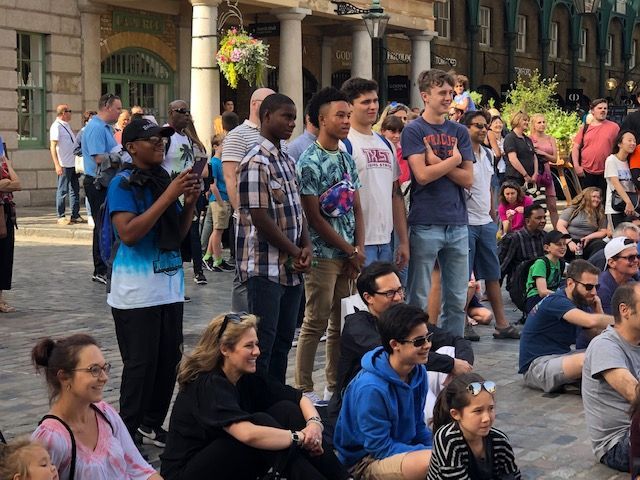 A group of people are sitting on the ground in front of a building.