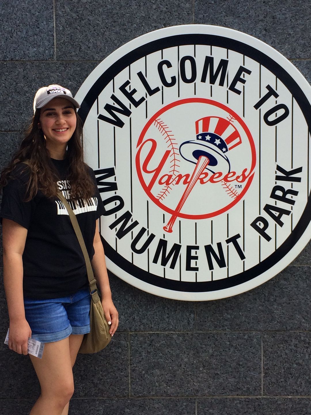 A woman is standing in front of a welcome to yankees monument sign