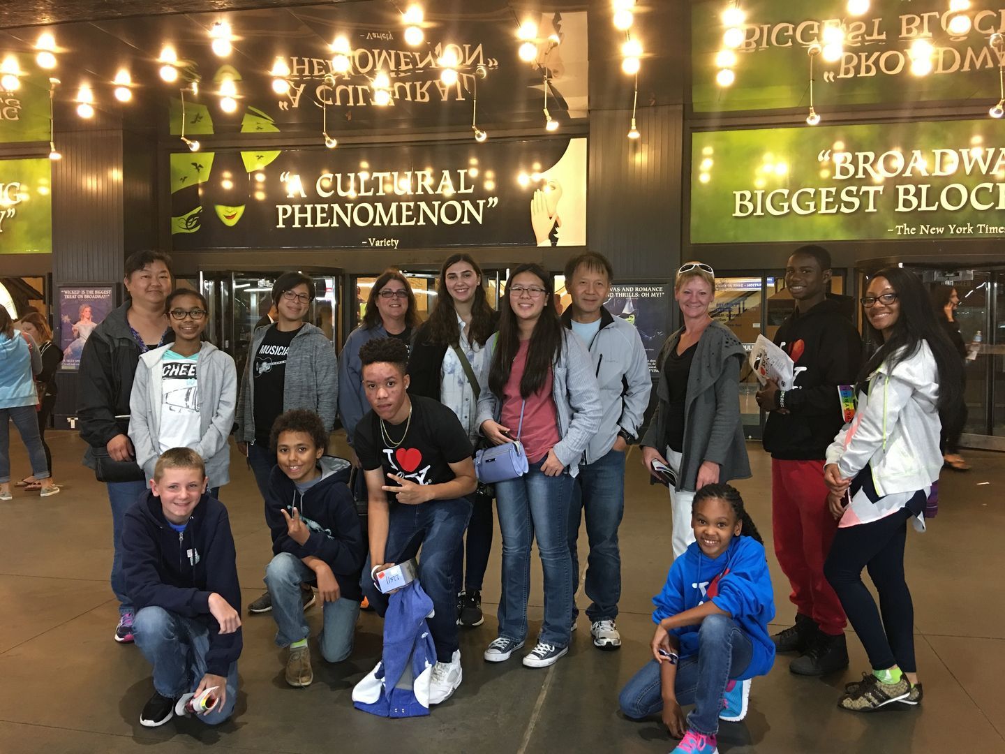 A group of people are posing for a picture in front of a broadway sign.