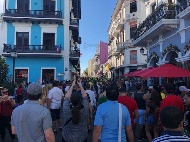 A crowd of people are walking down a street in front of a blue building.