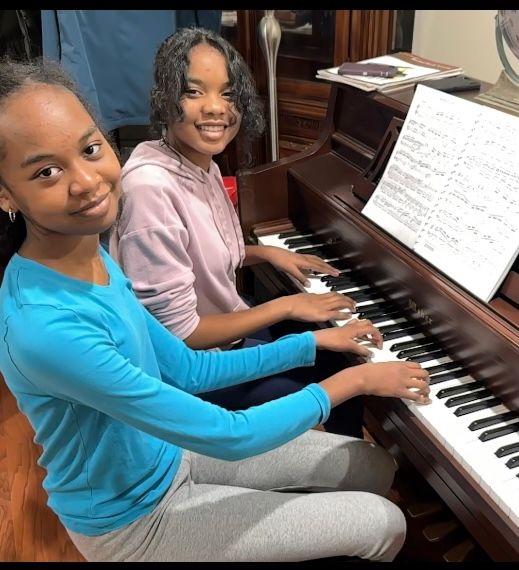 Two young girls are sitting at a piano with sheet music on it