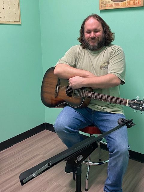 A man is sitting on a stool holding an acoustic guitar