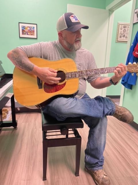 A man is sitting on a bench playing an acoustic guitar