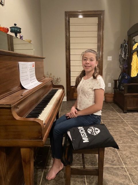 A young girl is sitting on a bench in front of a piano.