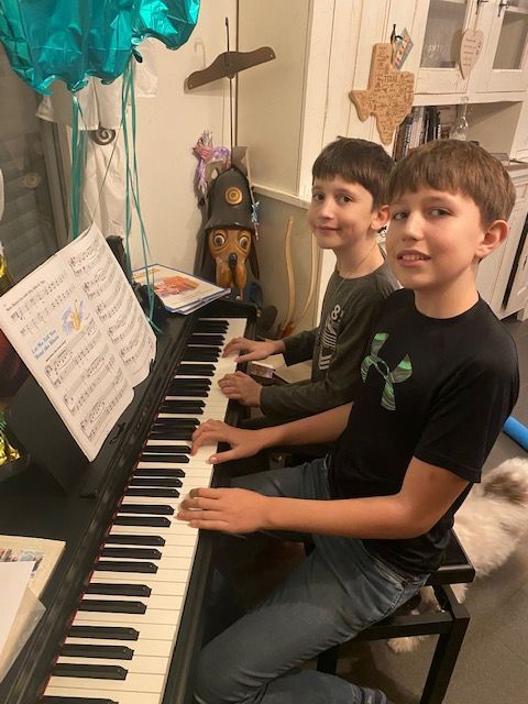 Two young boys are playing a piano in a living room