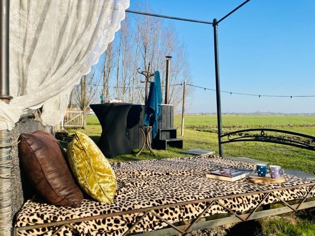 Ligbed voor buiten met luipaardprint, kussens en uitzicht op een groen veld.